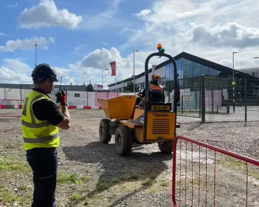 A trainer in hi-vis observing an operator driving a forward tipping dumper